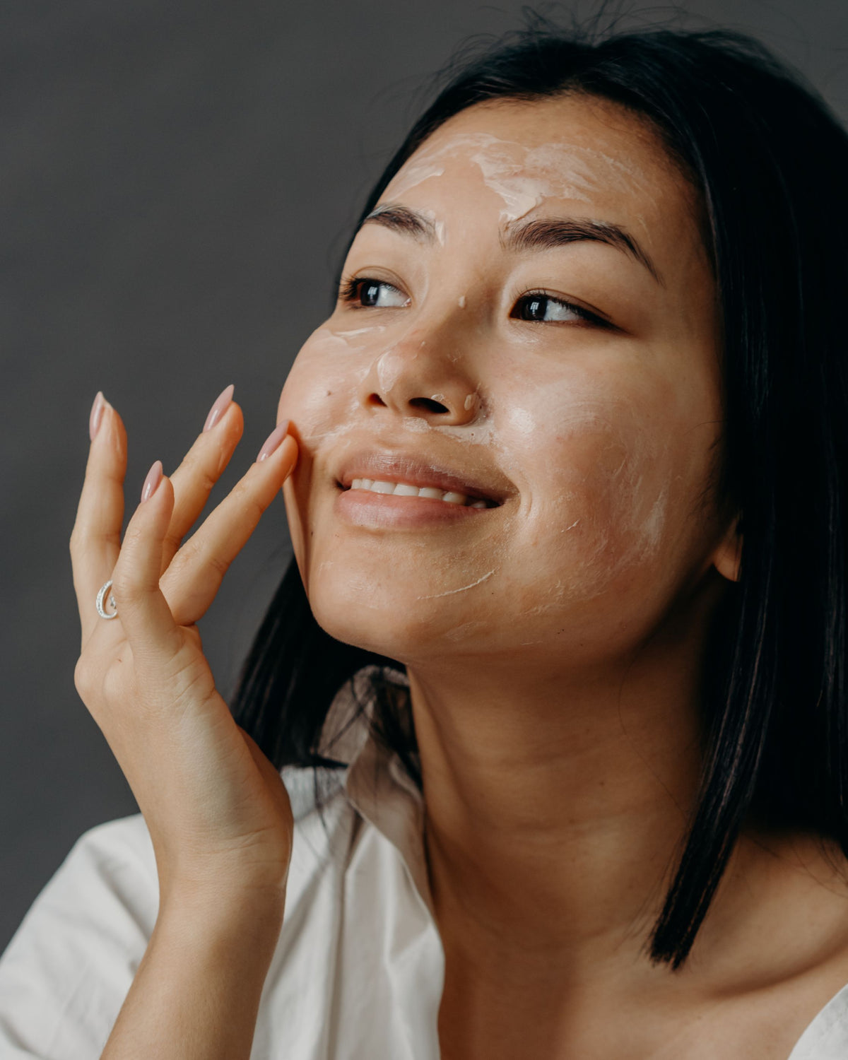 Chica asiática aplicándose crema facial con los dedos como parte de su rutina de cuidado de la piel