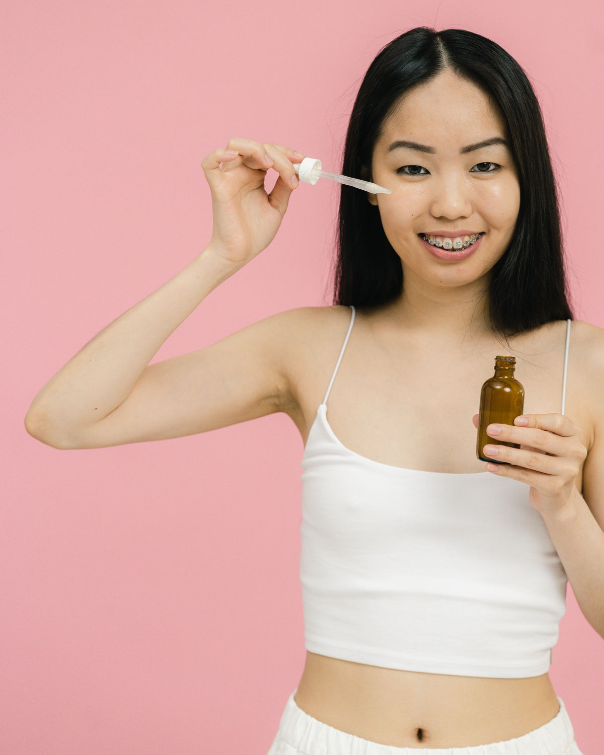 Chica asiática sonriente aplicándose un sérum con cuentagotas en el rostro