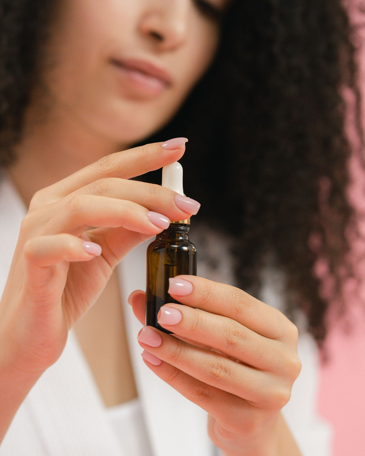 Chica asiática sosteniendo un frasco de sérum con cuentagotas sobre fondo rosa