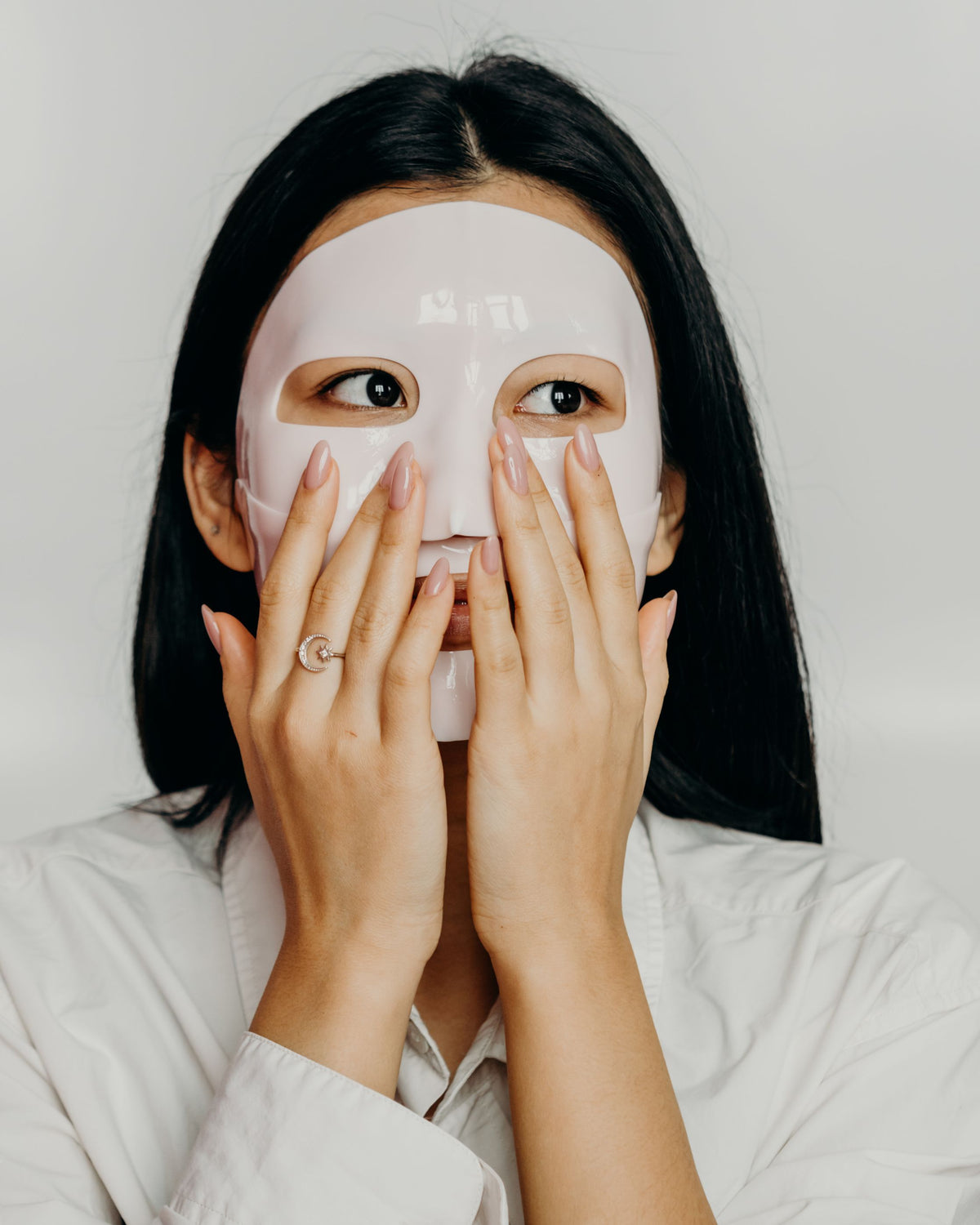 Chica asiática con mascarilla facial y las manos en las mejillas durante su rutina de cuidado de la piel